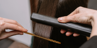 Stylist Straightening Hair Stylist straightening a brunette woman's hair with a flat iron during a keratin treatment