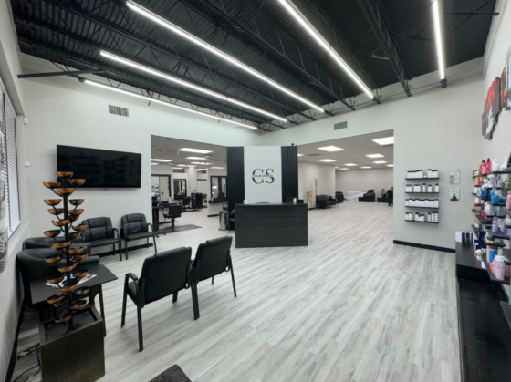 Photo of the newly remodeled lobby at The Color Studio and Salon showing gray wood grain flooring, black chairs, a black reception desk, and a wall of hair products on the right.