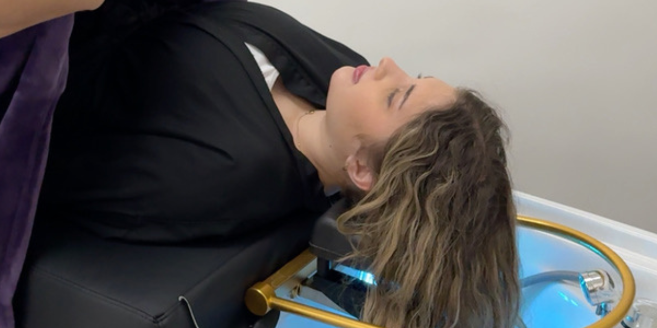 A woman lying on a Japanese head spa bed, being covered with a blanket by a stylist to ensure comfort during her spa treatment. The setting is serene, with a modern spa environment emphasizing relaxation and hair care.