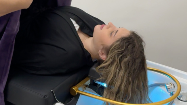 A woman lying on a Japanese head spa bed, being covered with a blanket by a stylist to ensure comfort during her spa treatment. The setting is serene, with a modern spa environment emphasizing relaxation and hair care.