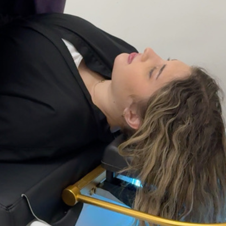 A woman lying on a Japanese head spa bed, being covered with a blanket by a stylist to ensure comfort during her spa treatment. The setting is serene, with a modern spa environment emphasizing relaxation and hair care.