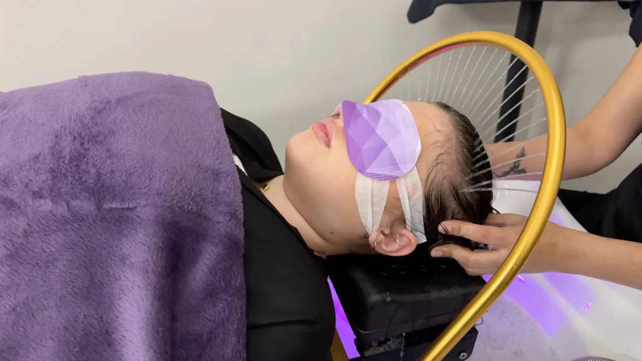Japanese Head Spa: A Path to Relaxation and Wellness 1 A young woman relaxes during a Japanese head spa treatment, lying back with a lavender eye mask. Her hair is thoroughly washed and massaged by a professional using two hands, under multiple streams of water from a modern halo enhancing the serene experience.